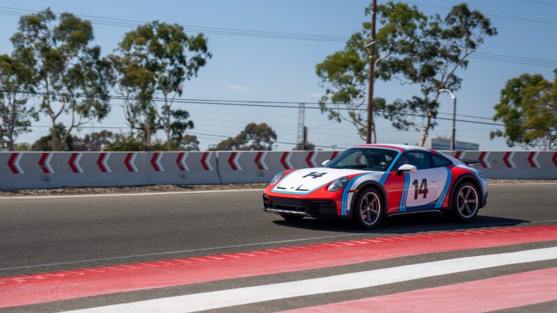 A race car with the number 14 drives on a track. Trees and a barrier with arrows are in the background.