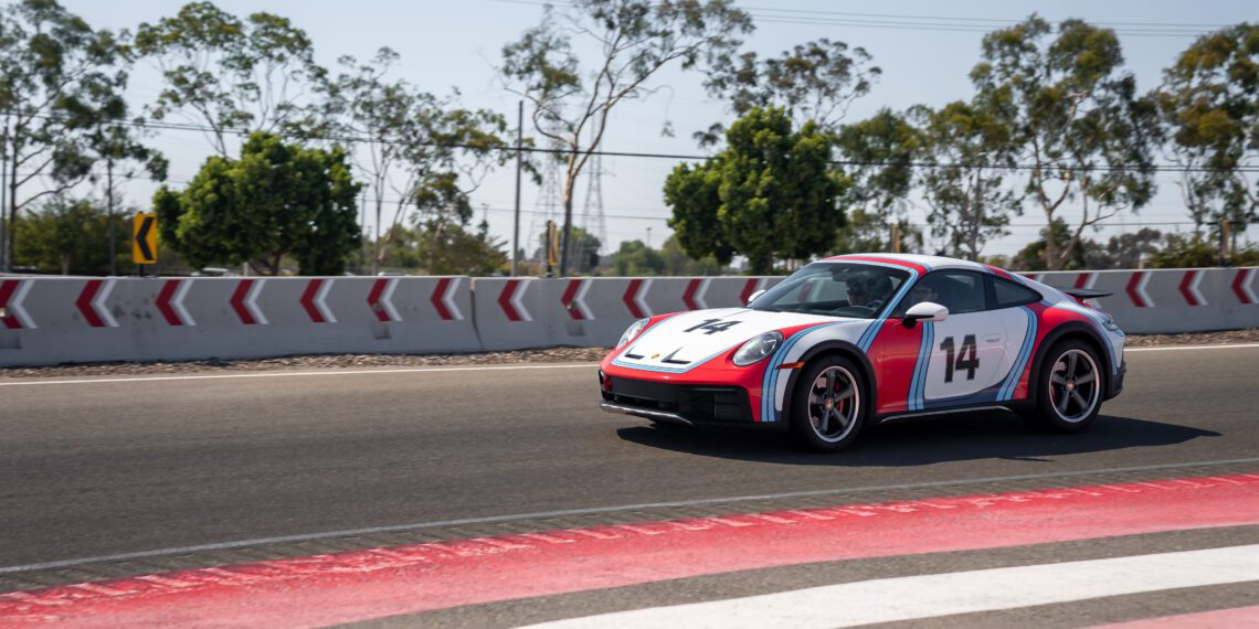 A sports car with the number 14 is racing on a track with trees and barriers in the background.