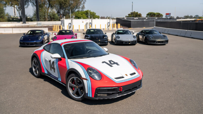 A group of six sports cars in a parking lot, with the front car having a number 14 and multicolored stripes.