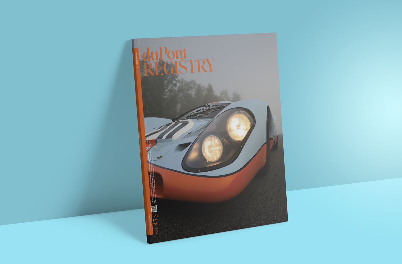 A duPont REGISTRY Gift Guide Edition magazine, dated December 2024, showcases a vintage racing car in striking blue and orange on its cover, elegantly propped against a light blue backdrop.