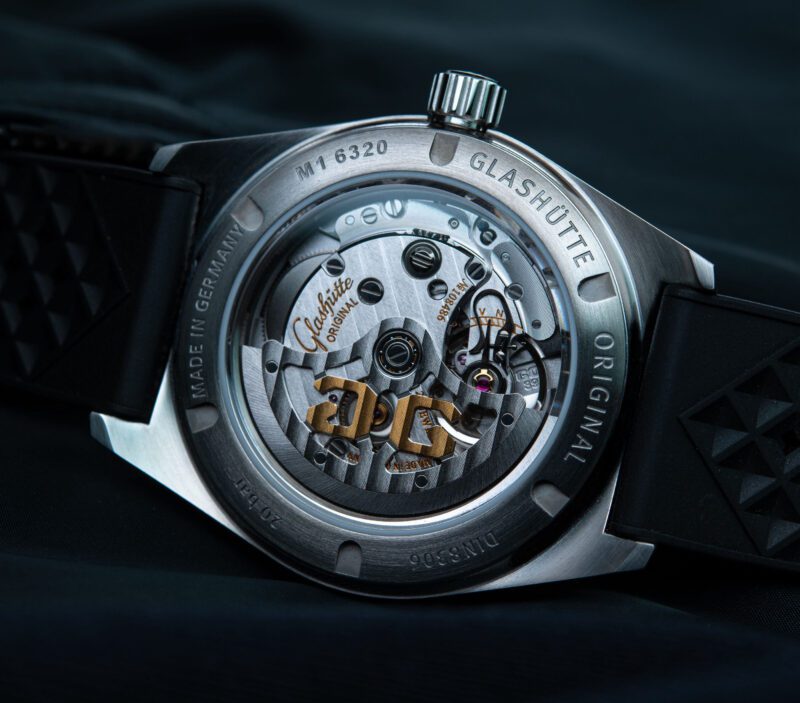 Close-up of the SeaQ Series watch's sapphire crystal case back, showcasing the intricate mechanical movement inside. The engravings and visible rotor are adorned with gold accents, a hallmark of Glashütte Original, standing out against a dark background.