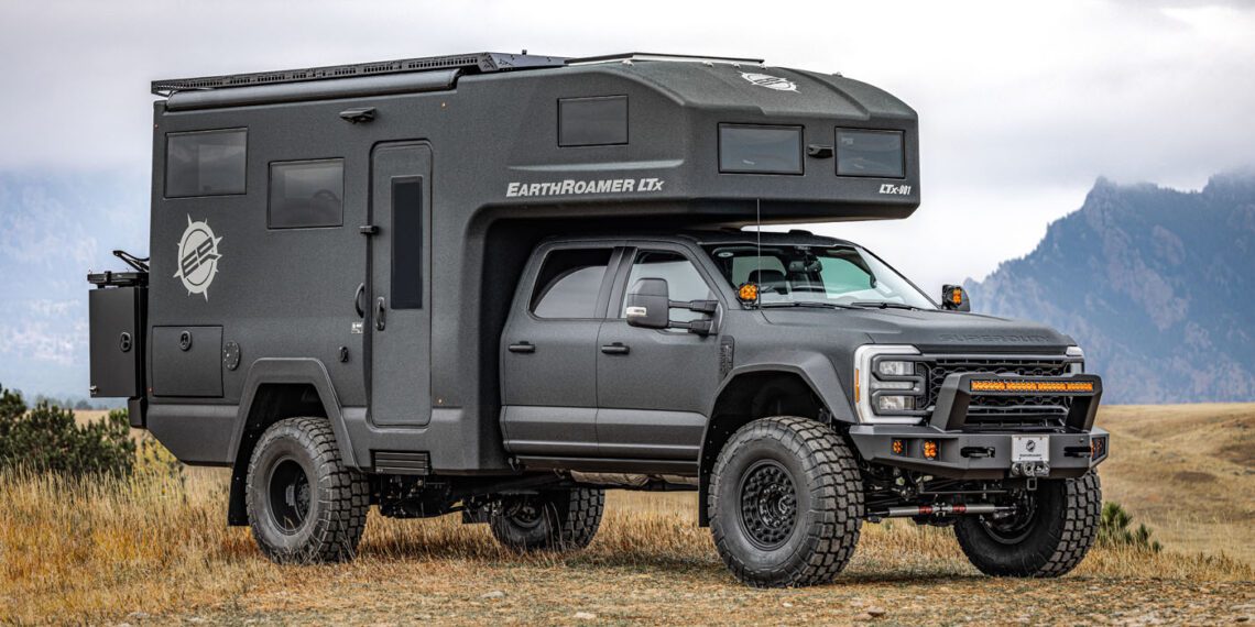 The ultimate expedition vehicle, an EarthRoamer with large tires and a rugged exterior, is parked on grassy terrain with majestic mountains in the background.