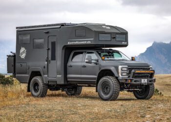 The ultimate expedition vehicle, an EarthRoamer with large tires and a rugged exterior, is parked on grassy terrain with majestic mountains in the background.
