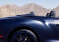 Side view of a dark blue convertible Bentley from Rancho Mirage with the top down, set against a backdrop of mountain peaks and a clear sky. The car's design showcases expressions of texture that enhance its elegance amidst nature's grandeur.