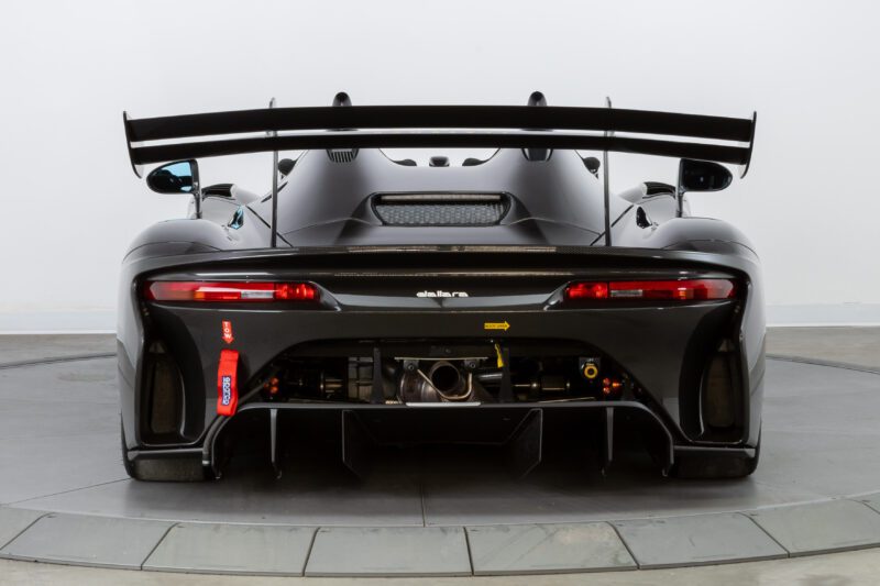 Rear view of a sleek black sports car with the Flatrock Ultimate Package, featuring a prominent spoiler, visible exhaust system, and red and yellow accents. This $2 Million Experience perfectly marries speed and elegance.