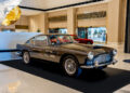 A classic black vintage car, possibly an Aston Martin, on display in an elegant indoor setting in Las Vegas, with a red car partially visible in the background.