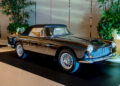 A classic black Aston Martin with chrome accents and wire-spoke wheels is displayed indoors at Fontainebleau Las Vegas, surrounded by plants and subtle lighting.