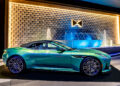 An Aston Martin in vibrant green is showcased indoors, set against a geometric textured wall with an illuminated fountain and reminiscent of a luxurious Las Vegas car collection.