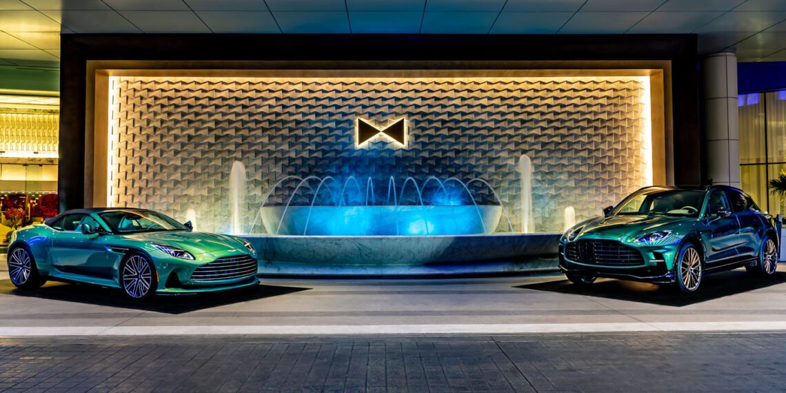 Two green Aston Martin cars from an exquisite car collection are parked in front of a large, illuminated fountain, capturing the vibrant spirit of Las Vegas at night.