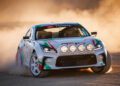 A Toyota adventure concept, part of the 2024 SEMA Lineup, showcases a sports car with a vibrant white, green, and red design as it roars down the dirt track, kicking up clouds of dust with its multiple round headlights blazing through.