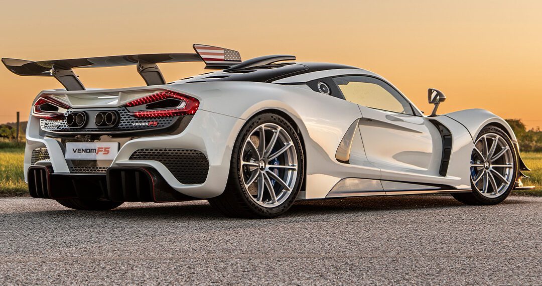 Sleek white sports car with aerodynamic design, prominent rear wing, and alloy wheels, reminiscent of the finest American supercars, parked on a paved road at sunset.