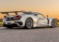 Sleek white sports car with aerodynamic design, prominent rear wing, and alloy wheels, reminiscent of the finest American supercars, parked on a paved road at sunset.