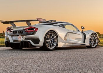Sleek white sports car with aerodynamic design, prominent rear wing, and alloy wheels, reminiscent of the finest American supercars, parked on a paved road at sunset.