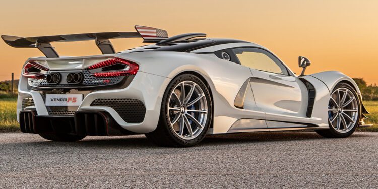 Sleek white sports car with aerodynamic design, prominent rear wing, and alloy wheels, reminiscent of the finest American supercars, parked on a paved road at sunset.