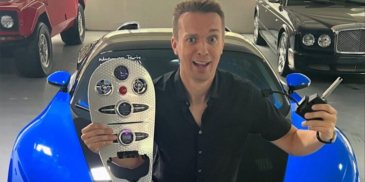 A person holds a car key and panel, sitting on a blue-and-black sports car in a garage filled with luxury cars, including a stunning 2008 Bugatti Veyron from Chicago Motor Cars.