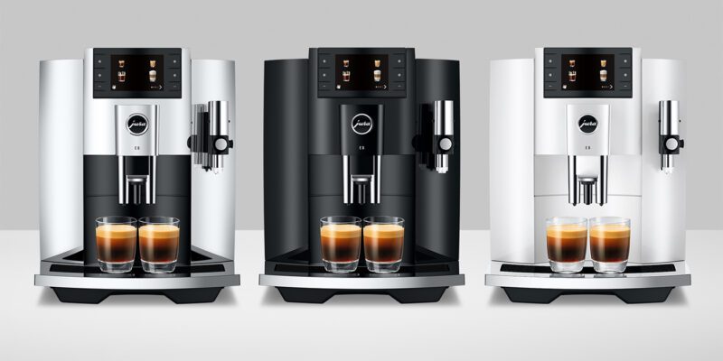 Three luxury coffee machines are lined up, each making two espresso shots. The sleek devices in silver, black, and white are perfect for coffee aficionados and make an ideal holiday gift.