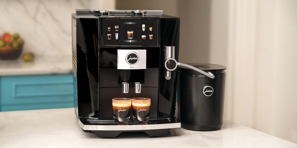 A black Jura coffee machine, a dream for coffee aficionados, stands on the kitchen counter with an attached milk container, skillfully dispensing two espresso shots into clear glasses.