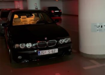 A sleek black BMW M5 is parked in a dimly lit parking garage, its interior beautifully illuminated like the cockpit of a hypercar.