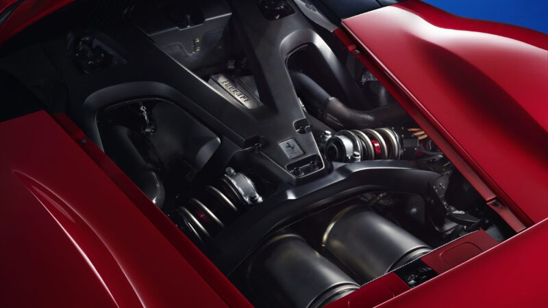 Close-up of a Ferrari F80's engine compartment, showcasing intricate mechanical components and the iconic logo on the engine cover. The vehicle's hood is painted red, hinting at the power and specs that justify its premium price tag.