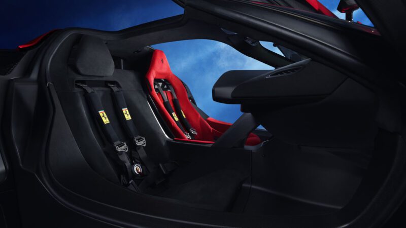 The interior of the Ferrari F80 sports car features two red racing seats with harnesses, set against a sleek black and blue background.