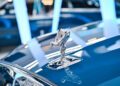 In an opulent Abu Dhabi showroom, a close-up reveals a silver hood ornament shaped like a winged figure, gracefully adorning the shiny blue Rolls-Royce.