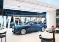 A blue Rolls-Royce luxury sedan is elegantly displayed in a modern showroom in Abu Dhabi, with beautiful floral arrangements adorning nearby tables.