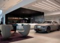 A luxury Rolls-Royce is parked in a sleek, modern showroom in Abu Dhabi, surrounded by contemporary furniture with a long bar elegantly adorning the background.