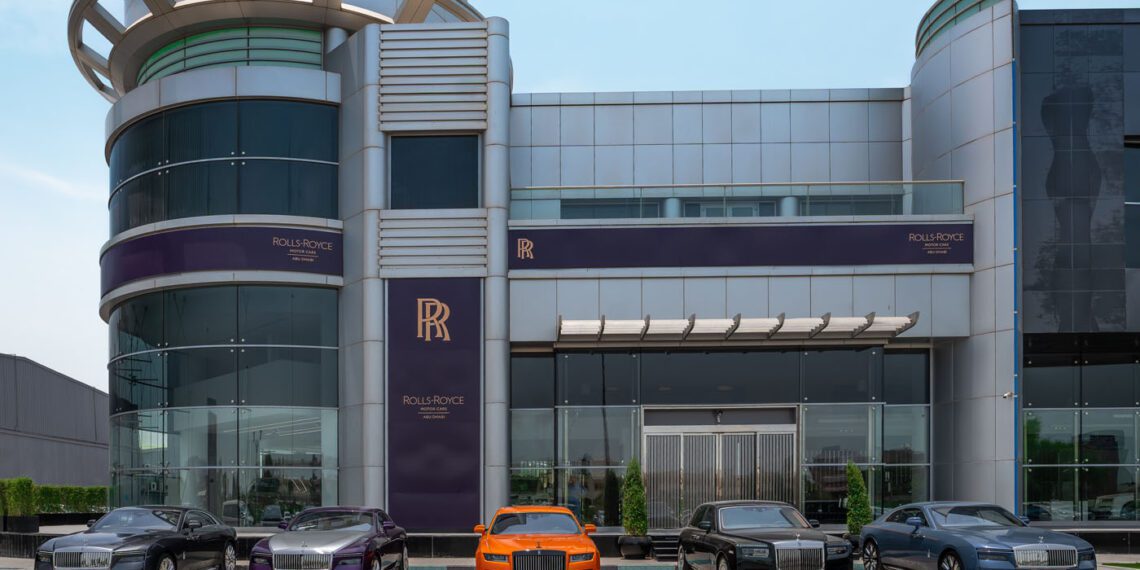 A luxury car dealership in Abu Dhabi showcases five Rolls-Royce cars parked in front of a modern glass and metal showroom.