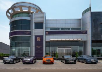 A luxury car dealership in Abu Dhabi showcases five Rolls-Royce cars parked in front of a modern glass and metal showroom.