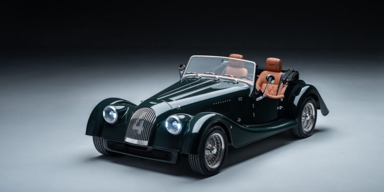A classic green Morgan convertible car with brown leather seats, wire wheels, and a vintage design, the Plus Four is elegantly displayed in a studio setting.