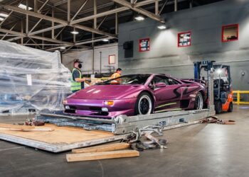 The Lamborghini Diablo SV in striking Viola 30th is positioned on a platform inside a CURATED warehouse. Nearby, two workers and a forklift stand ready to assist.
