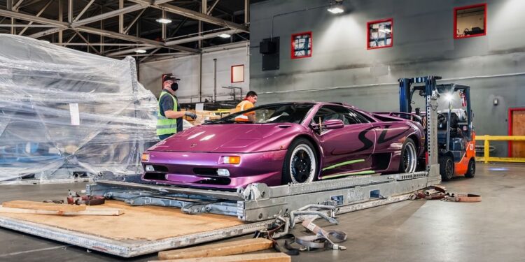 The Lamborghini Diablo SV in striking Viola 30th is positioned on a platform inside a CURATED warehouse. Nearby, two workers and a forklift stand ready to assist.