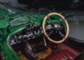 Interior view of a vintage Bentley Speed Six from the Continuation Series, featuring a wooden steering wheel and a dashboard full of dials. Complete with a fire extinguisher and red leather seats, this classic car exudes timeless elegance and style.