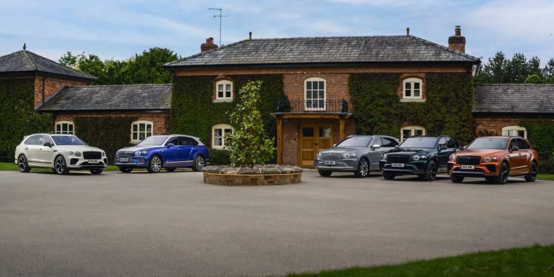 Six cars, including a sleek Bentley, are parked in front of a brick house with ivy-covered walls and a paved driveway. The setting evokes the sophistication of The Mews and promises a refined client experience.