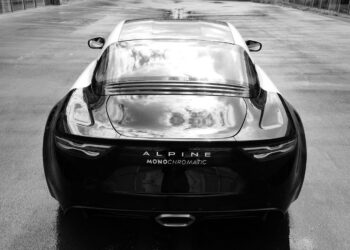 The sleek Black Alpine A110 sports car, an Art Car masterpiece, proudly displays "Monochromatic" on its rear. It's parked on a glistening wet road, viewed from behind in stunning elegance.