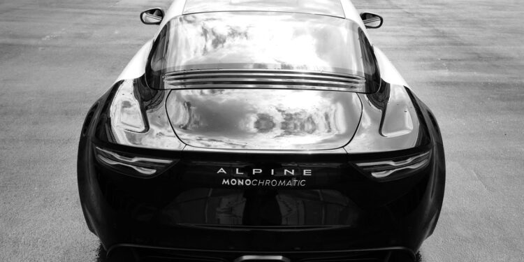 The sleek Black Alpine A110 sports car, an Art Car masterpiece, proudly displays "Monochromatic" on its rear. It's parked on a glistening wet road, viewed from behind in stunning elegance.