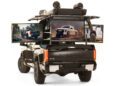 A black 2024 Toyota Tundra with a rooftop tent showcases its Adventure Concepts, featuring two mounted screens that display images of the truck in stunning outdoor settings.