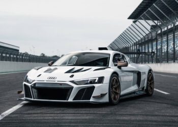 A white ABT XGT race car is parked on a racetrack in the United States, surrounded by fencing and grandstands.