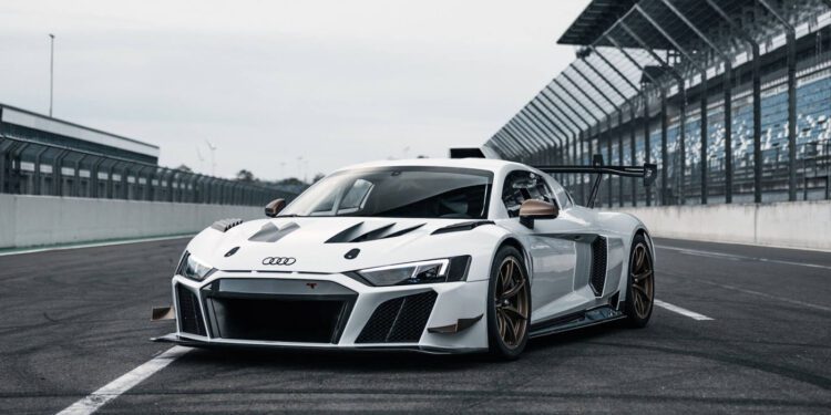 A white ABT XGT race car is parked on a racetrack in the United States, surrounded by fencing and grandstands.