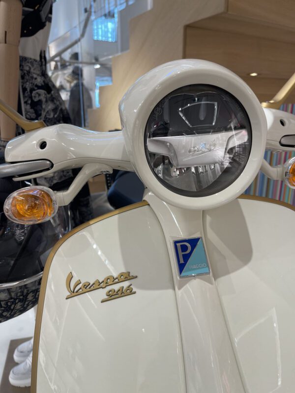 Close-up of a white Vespa scooter's front, showing the headlight and Vespa 946 logo, inside a store.