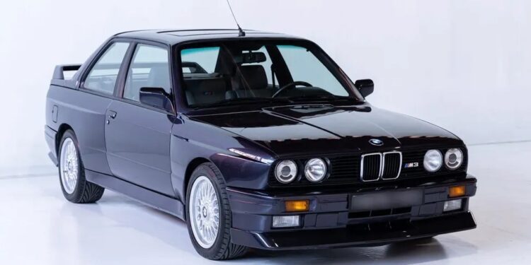 A black classic BMW M3 car, reminiscent of a German heavy metal band's power, is parked in a pristine white studio, viewed from the front-left angle.
