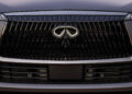 Close-up of a car's front grille, showcasing an Infiniti logo with a stylized "A" or "V" shape and sharp, angular designs. This epitome of tailgating luxury blends sophistication with dynamic flair, evocative of an exclusive AUTOGRAPH Lounge experience.