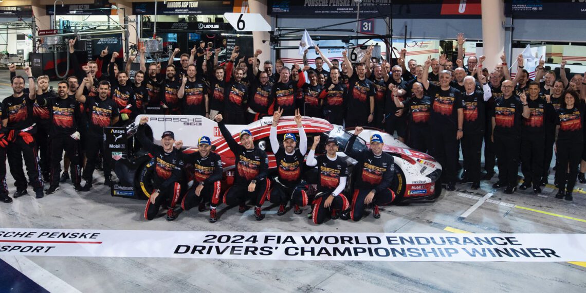 A racing team, comprised of accomplished works drivers, celebrates their FIA WEC 2024 World Endurance Championship win, posing triumphantly around a Porsche with arms raised in a cheering gesture.