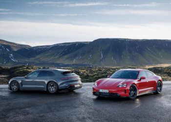 Two sleek Taycan 4 cars are parked on a wet road in a mountainous landscape under a cloudy sky.