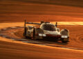 A Porsche race car takes a corner on a sunlit track, casting long shadows as it prepares for the FIA WEC 2024 with its skilled works drivers.