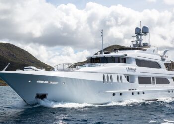 A large luxury yacht cruises through the water, offering a remarkable maritime experience with hilly islands in the background under a cloudy sky.