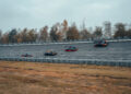 Four Bugatti sports cars, including the W16 Mistral, race on a banked track with a forest in the background, pushing the limits of open-top speed records.