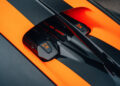 Close-up view of a Bugatti W16 Mistral engine cover with carbon fiber texture and striking orange and black detailing, showcasing W16 and Bugatti logos, representing the thrilling 282.05 MPH open-top speed record.