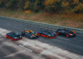 Four high-performance sports cars, including the Bugatti W16 Mistral known for its open-top speed record of 282.05 MPH, are parked in a line on a paved road, surrounded by trees with autumn foliage.