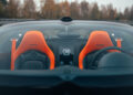 Front view of a Bugatti W16 Mistral sports car interior, featuring two orange seats with "Vitesse" labels and a circular logo on a central panel. Trees and sky are visible through the rear window, capturing the essence of its 282.05 MPH open-top speed record.